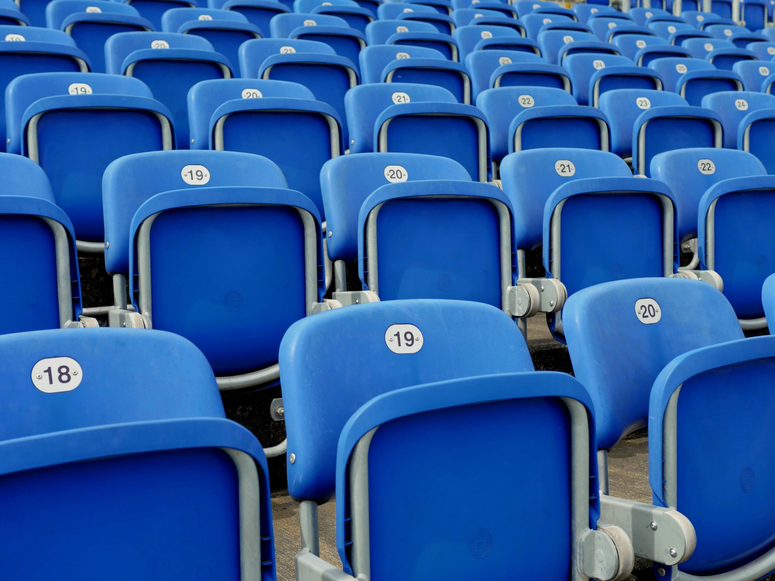 Rows of blue plastic stadium seats numbered and aligned perfectly in an empty grandstand.